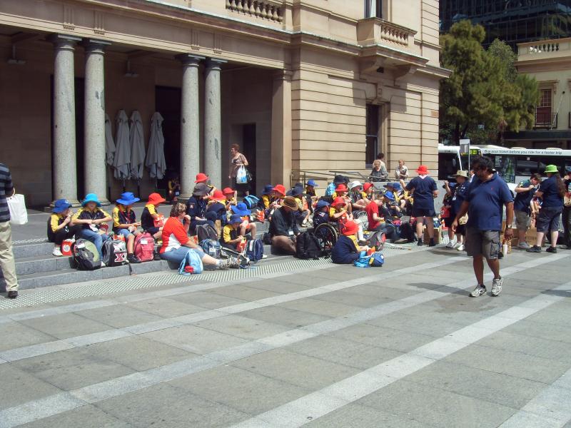 Children and adults sit together on steps in front of a historic building