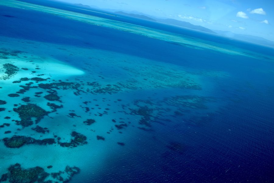 Luftaufnahme von türkisfarbenem Wasser und Riffstrukturen am Great Barrier Reef in Queensland.